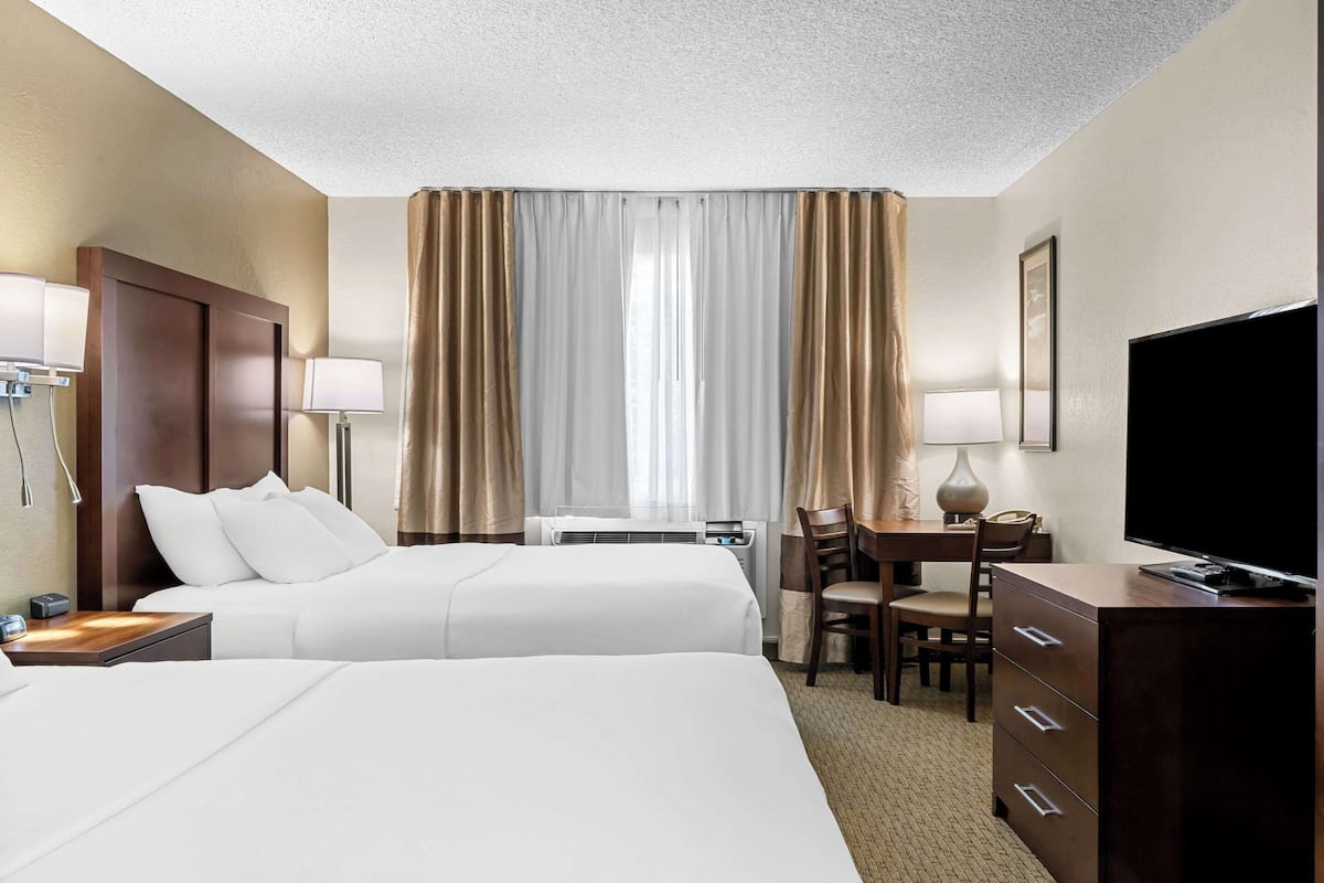 Ein Hotelzimmer mit zwei Betten, einem Schreibtisch mit Stuhl, einem Fernseher und einer Schreibtischlampe.
