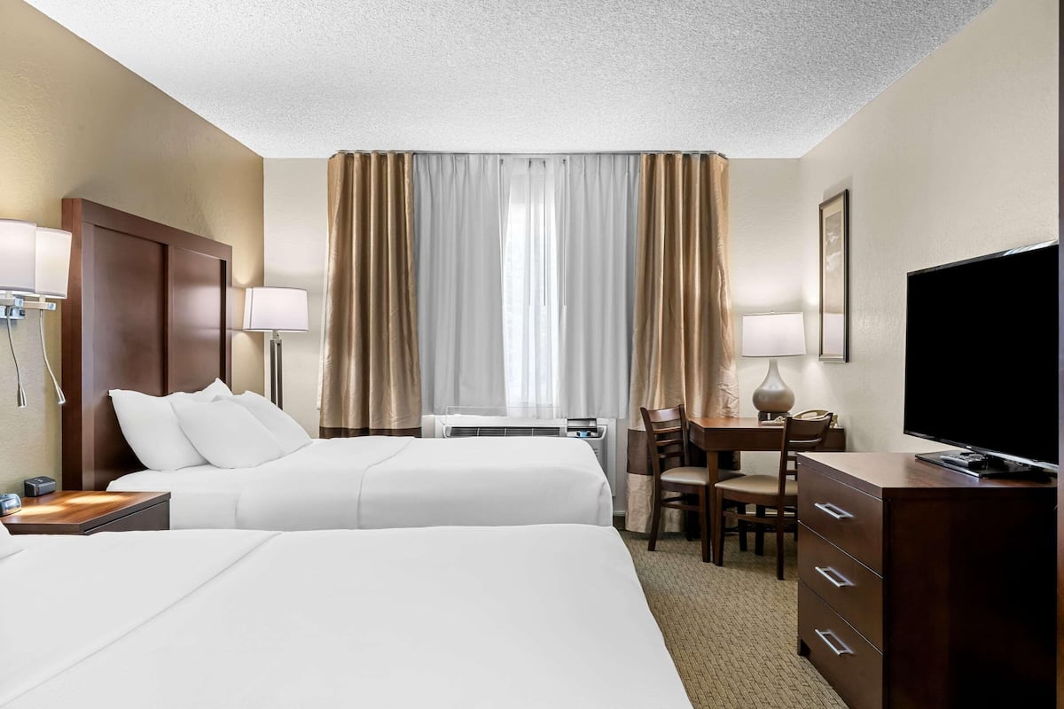 Ein Hotelzimmer mit zwei Betten, einem Schreibtisch, einem Sessel, einem Fernseher und einer Klimaanlage.