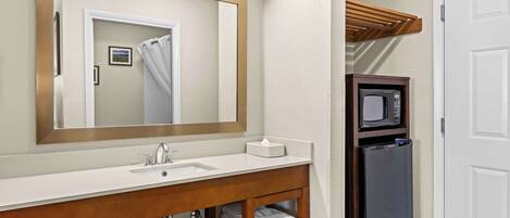A bathroom with a white sink, a mirror, a towel rack, and a microwave.