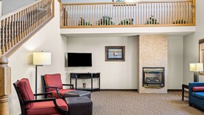 A spacious living area with a high ceiling, a fireplace, a television, and a balcony with a railing. - Comfort Inn Worland Hwy 16 to Yellowstone (Worland)