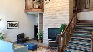 A spacious living room with a high ceiling, a chandelier, a staircase with a patterned carpet, and a flat-screen TV. - Country Inn & Suites by Radisson Bismarck Waterpark (Bismarck)