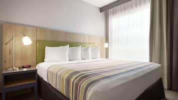 Hotellihuone, jossa on suuri sänky, kaksi yöpöytävalaisinta, puinen pääty ja ikkuna, jossa on verhot.