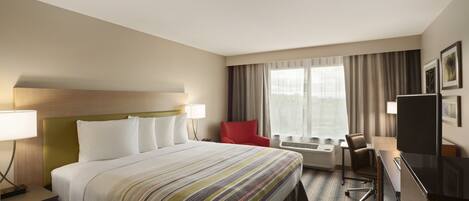 A hotel room with a large bed, a desk with a chair, a TV, and a window with curtains.