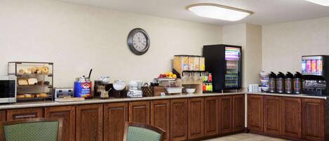 A breakfast bar with a clock, a microwave, a toaster, and a coffee machine.