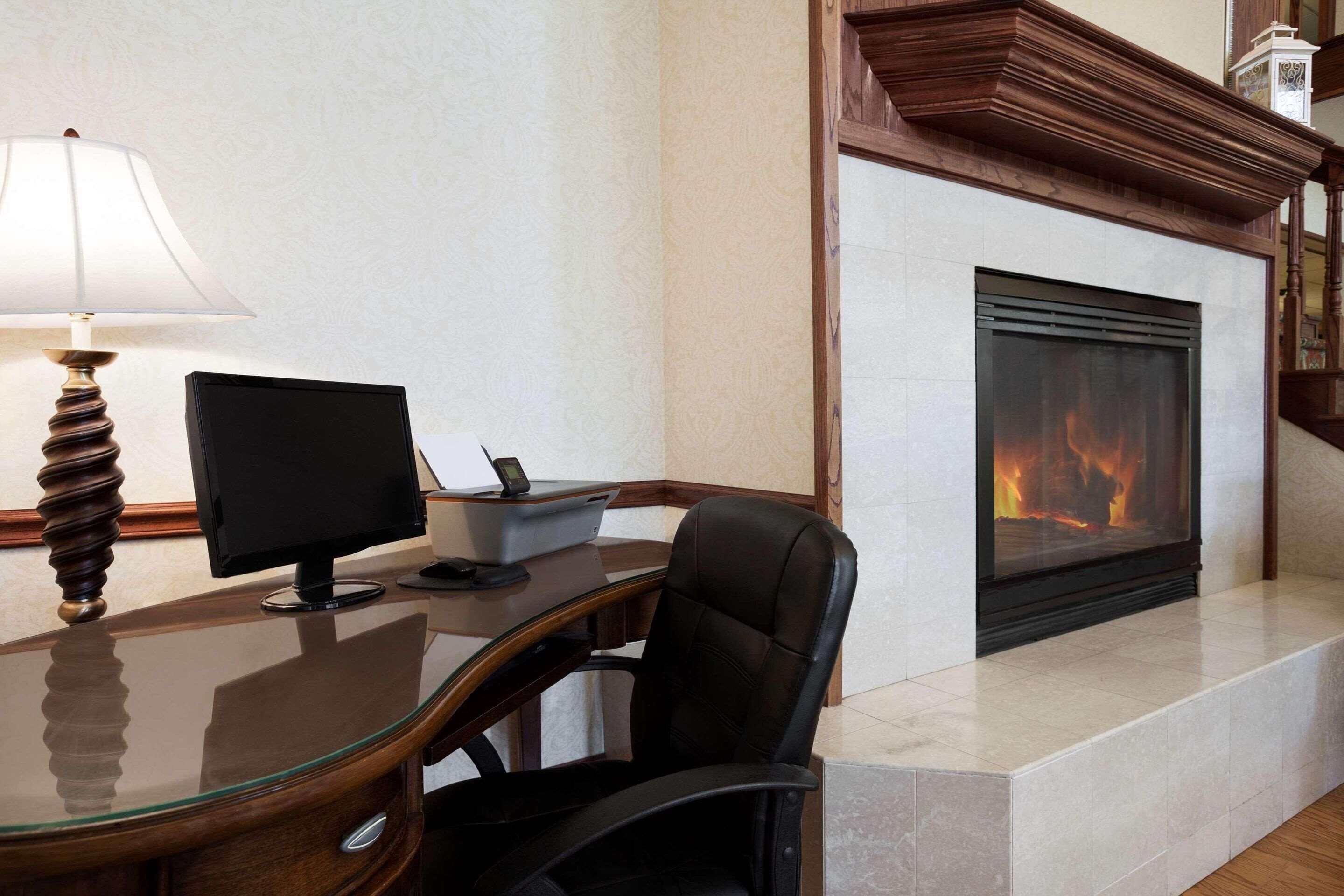 A modern office with a glass desk, a computer, and a fireplace.