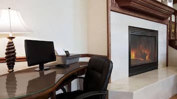 A modern office with a glass desk, a computer, and a fireplace.