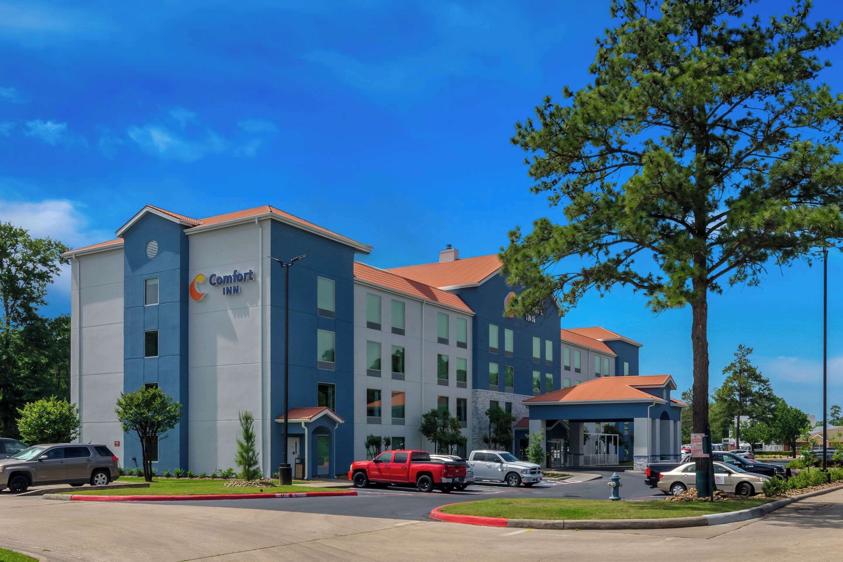 A Comfort Inn hotel with a modern design, featuring a mix of blue and gray exterior, multiple windows, and a parking lot with several vehicles.