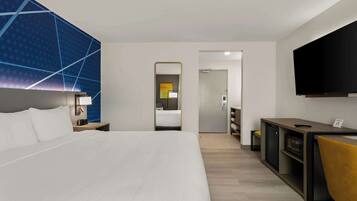A modern hotel room with a large bed, a desk with a flat-screen TV, a mirror, and a wardrobe.