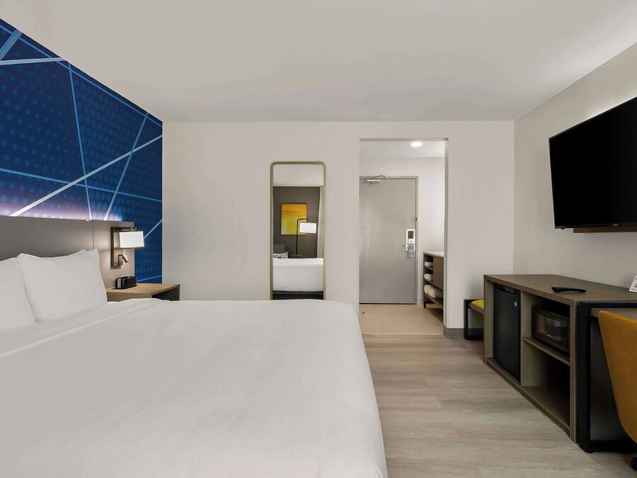 Habitació d'hotel moderna amb un llit gran, una escriptori amb televisió de pantalla plana, un mirall i un armari.