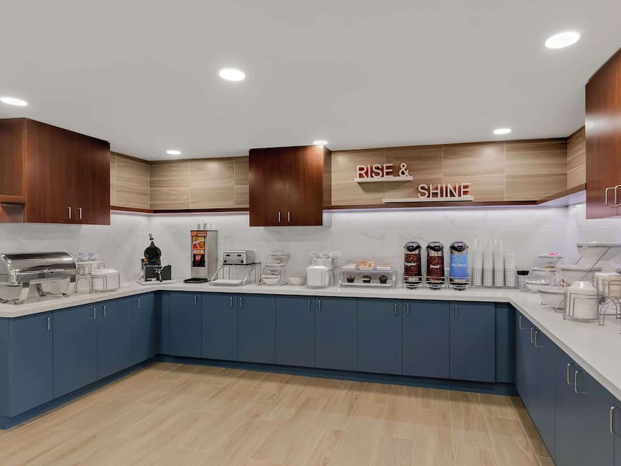 Una cocina moderna con armarios azules, encimera de mármol y varios electrodomésticos, incluyendo una cafetera y un calentador de alimentos.