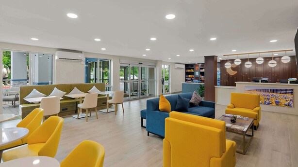 Un hall d’entrée moderne avec des sièges aux couleurs jaune et bleu, un comptoir d’accueil et de grandes fenêtres.