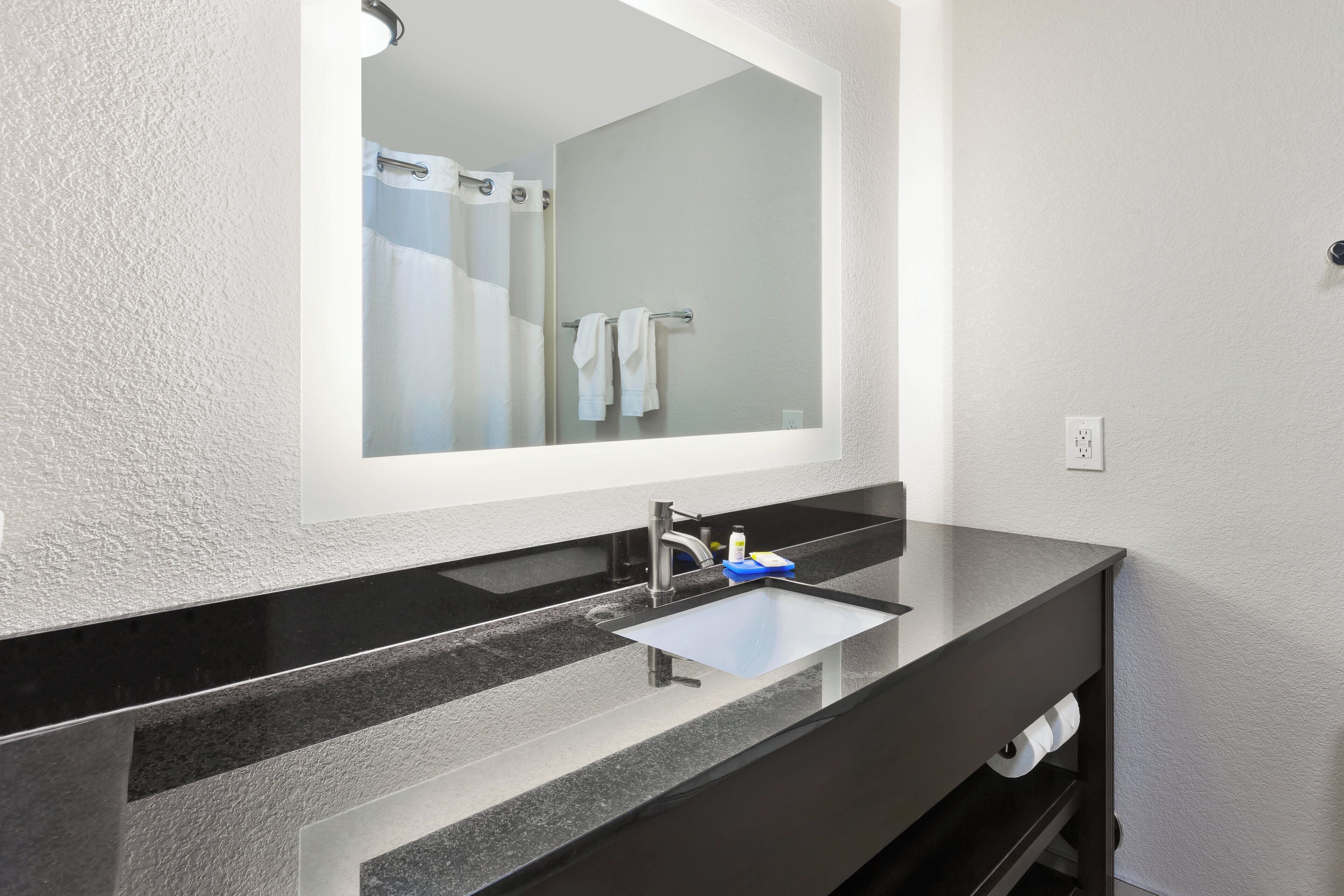 A bathroom with a large mirror, a black countertop, a sink, and a towel rack.
