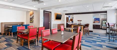 A hotel dining area with red chairs and a wooden table, a fireplace, and a television on the wall.
