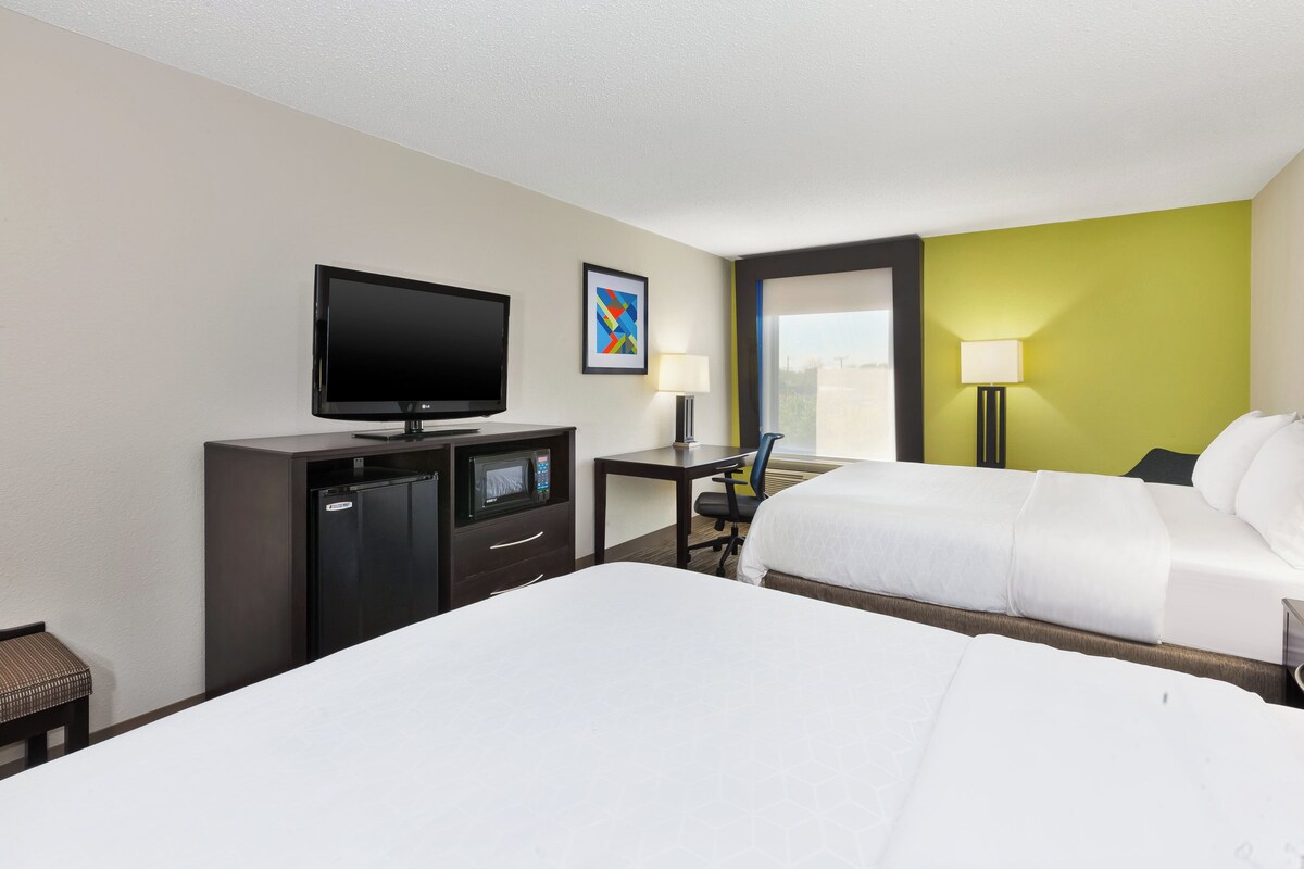 A hotel room with two beds, a desk with a computer, a television, a microwave, and a small seating area.