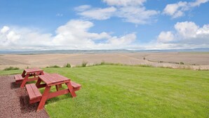Une table de pique-nique installée sur une pelouse, avec un ciel dégagé et des collines qui se dessinent à l’horizon.