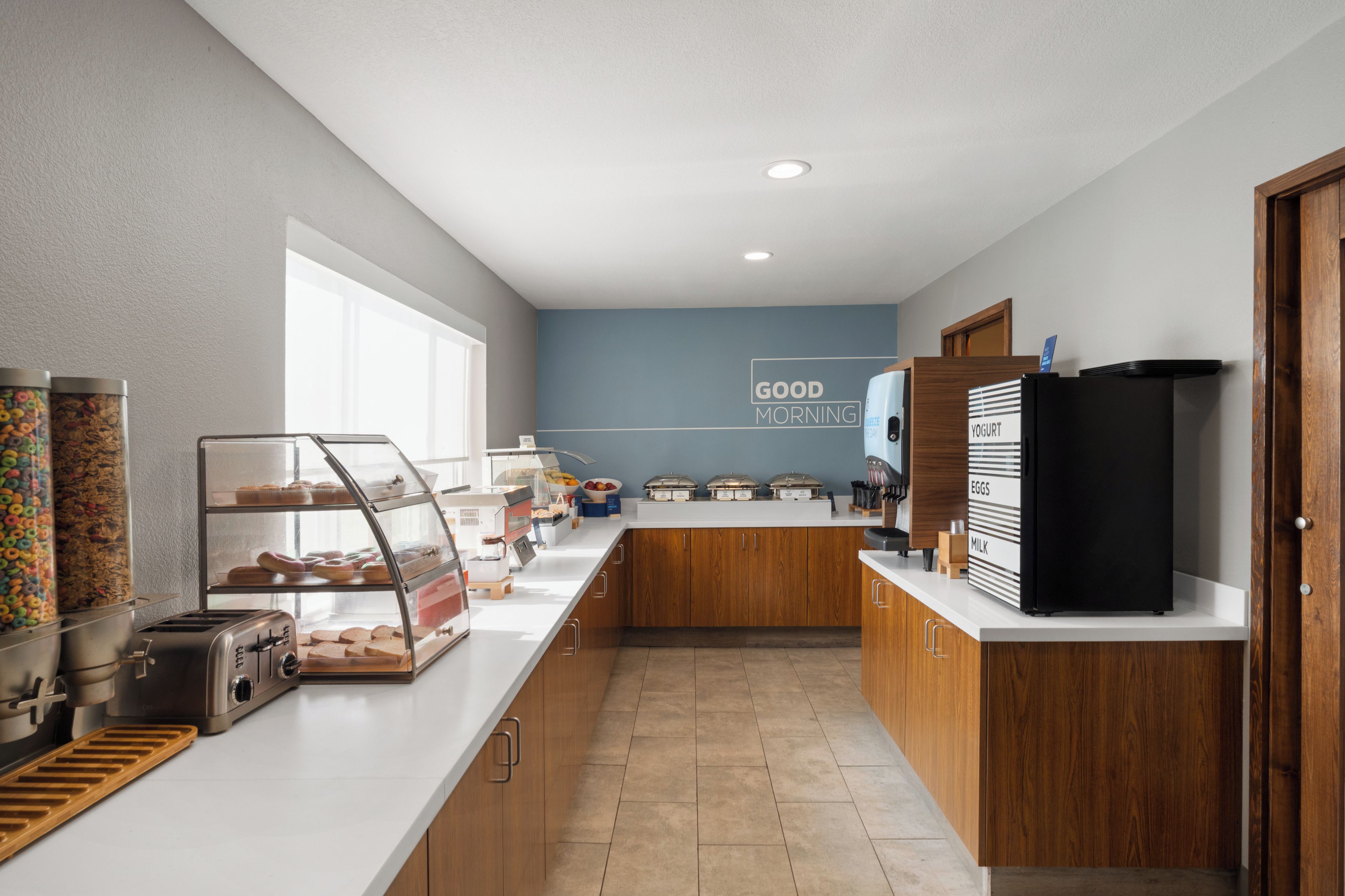A modern kitchen with a breakfast bar, a refrigerator, and a wall sign that says 'GOOD MORNING'.