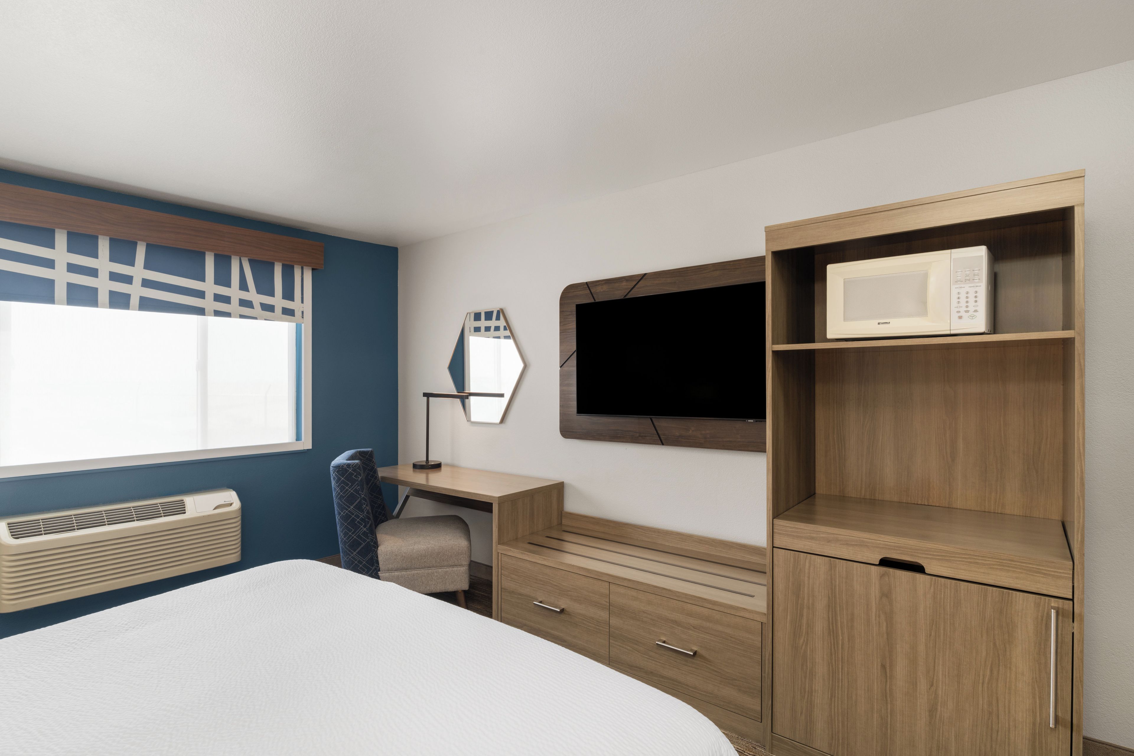 A bedroom with a bed, a desk, a chair, a TV, and a microwave.