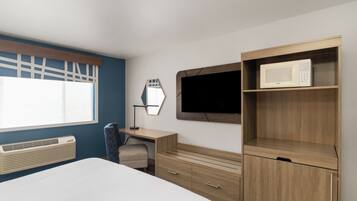 A bedroom with a bed, a desk, a chair, a TV, and a microwave.
