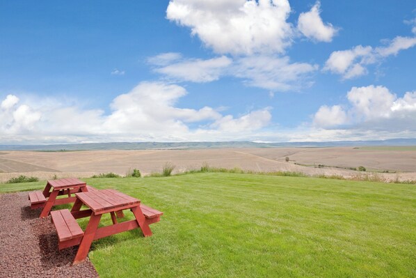 A picnic table set on a grassy field with a clear sky and distant hills.