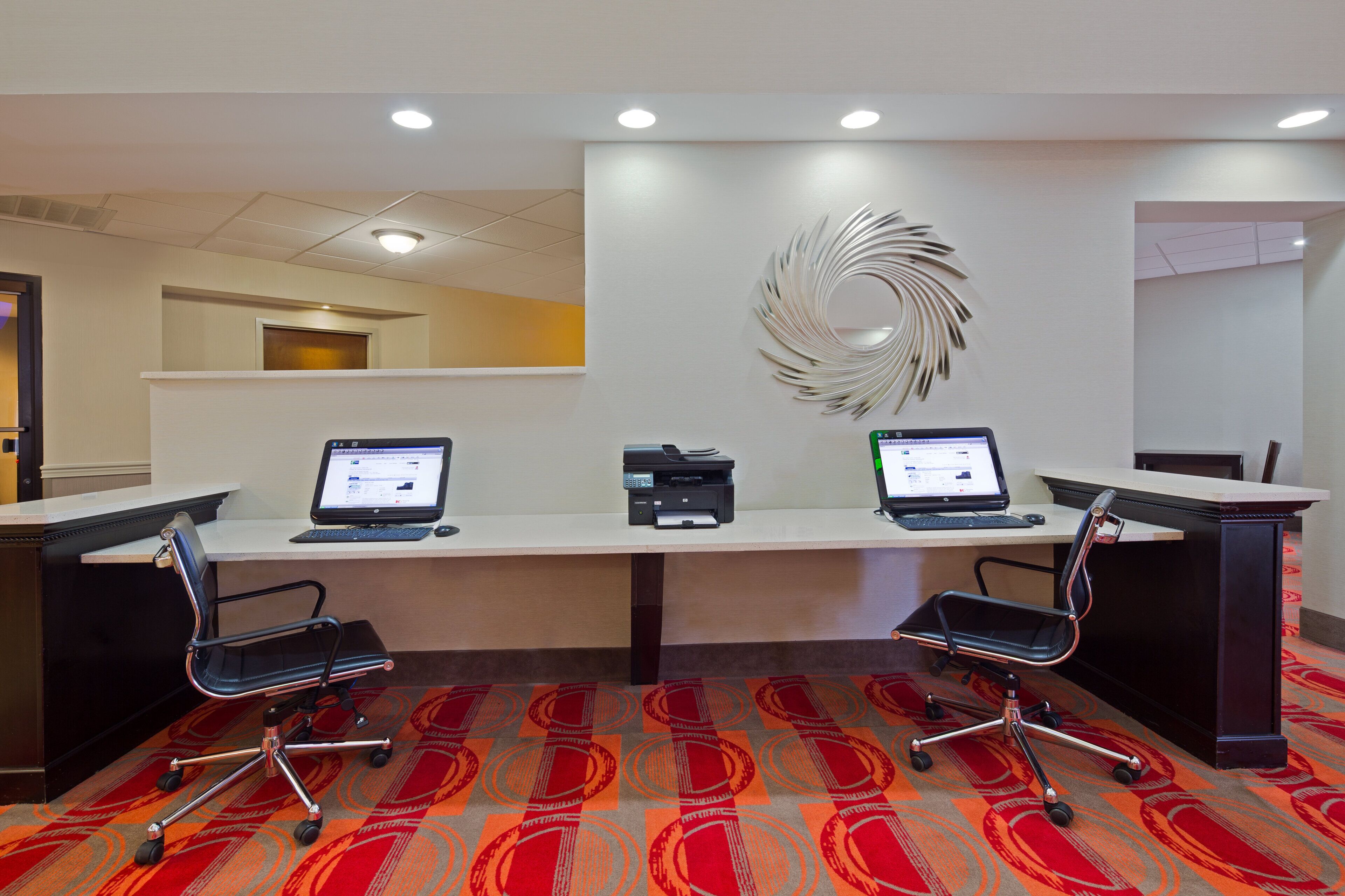A conference room with two desks, each with a laptop and a printer, and two office chairs.