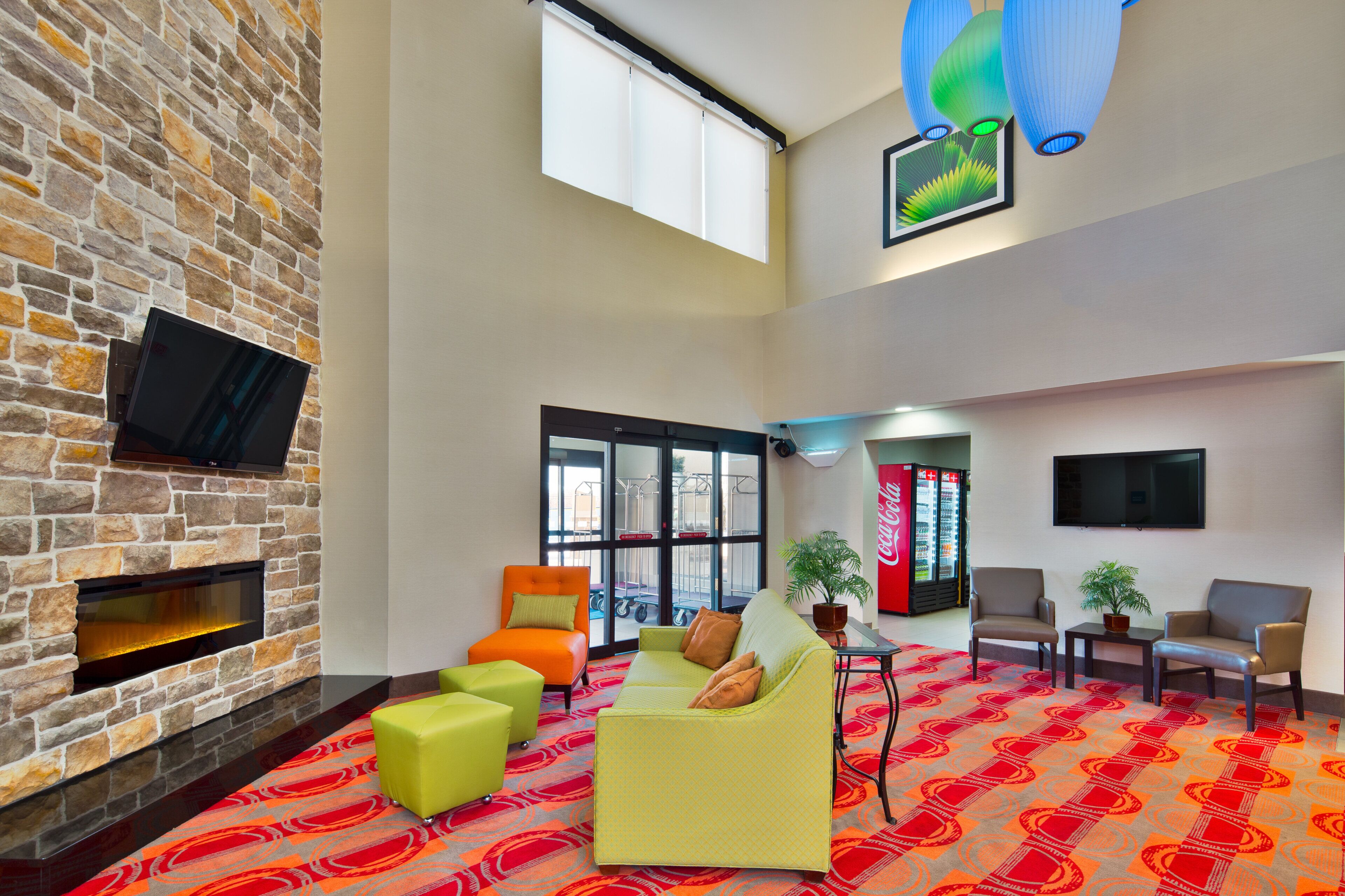 A spacious lobby with a stone wall, a fireplace, comfortable seating, a large window, and a Coca-Cola refrigerator.