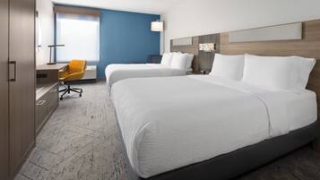 A hotel room with two beds, a desk with a chair, and a large window.