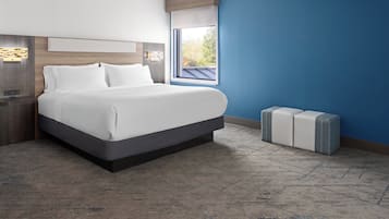 A modern hotel room with a large bed, a nightstand, a window with a view, and a built-in bench.