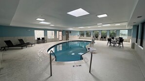 A large indoor swimming pool with lounge chairs and tables, surrounded by large windows. - Holiday Inn Express Harrisburg I-81 – Hershey by IHG (Harrisburg)