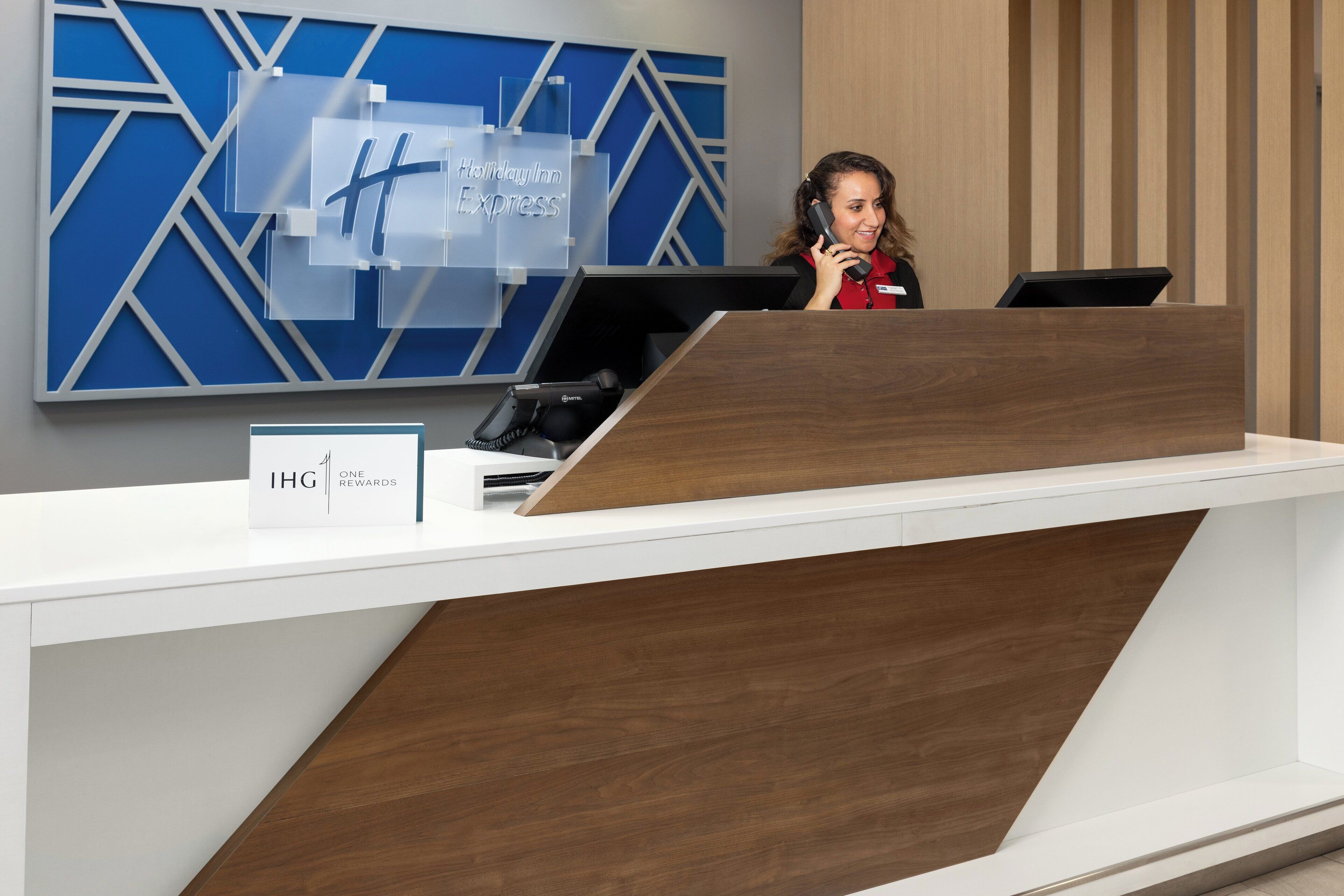Un comptoir d’accueil d’hôtel au design moderne, doté d’un écran numérique et d’une enseigne indiquant le programme de fidélité IHG Rewards.