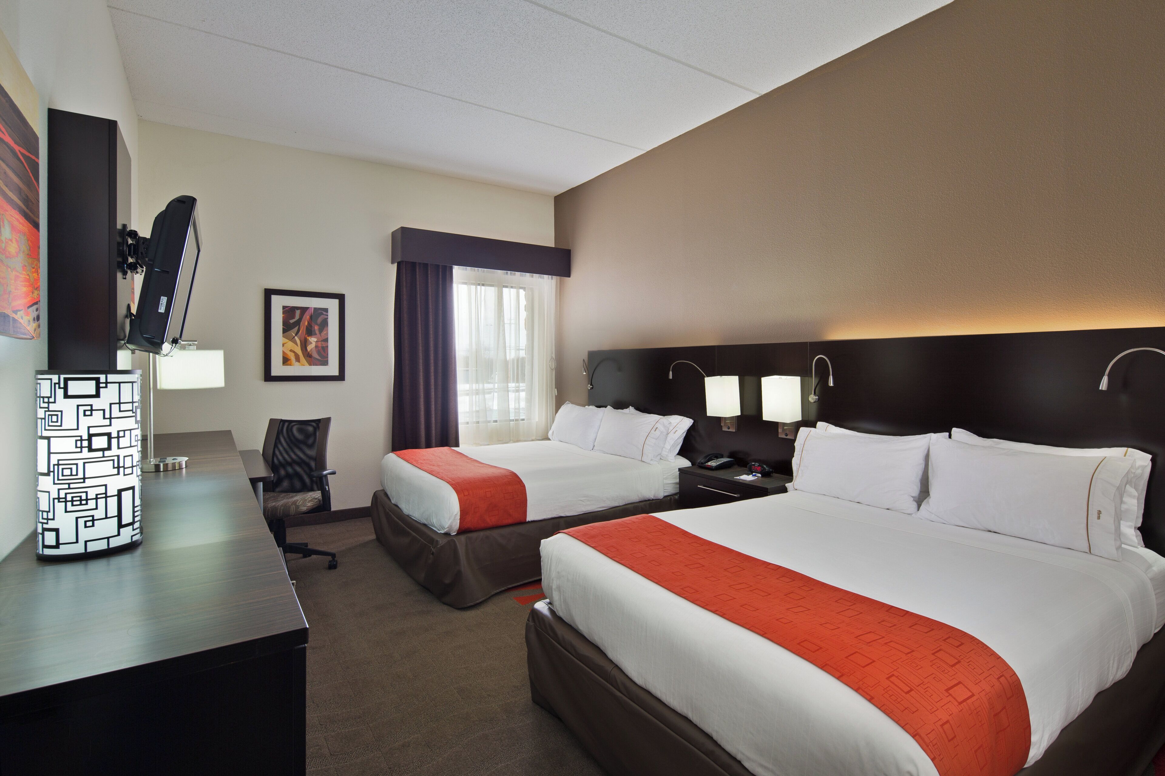 A hotel room with two beds, a desk, a chair, a TV, and a window with curtains.