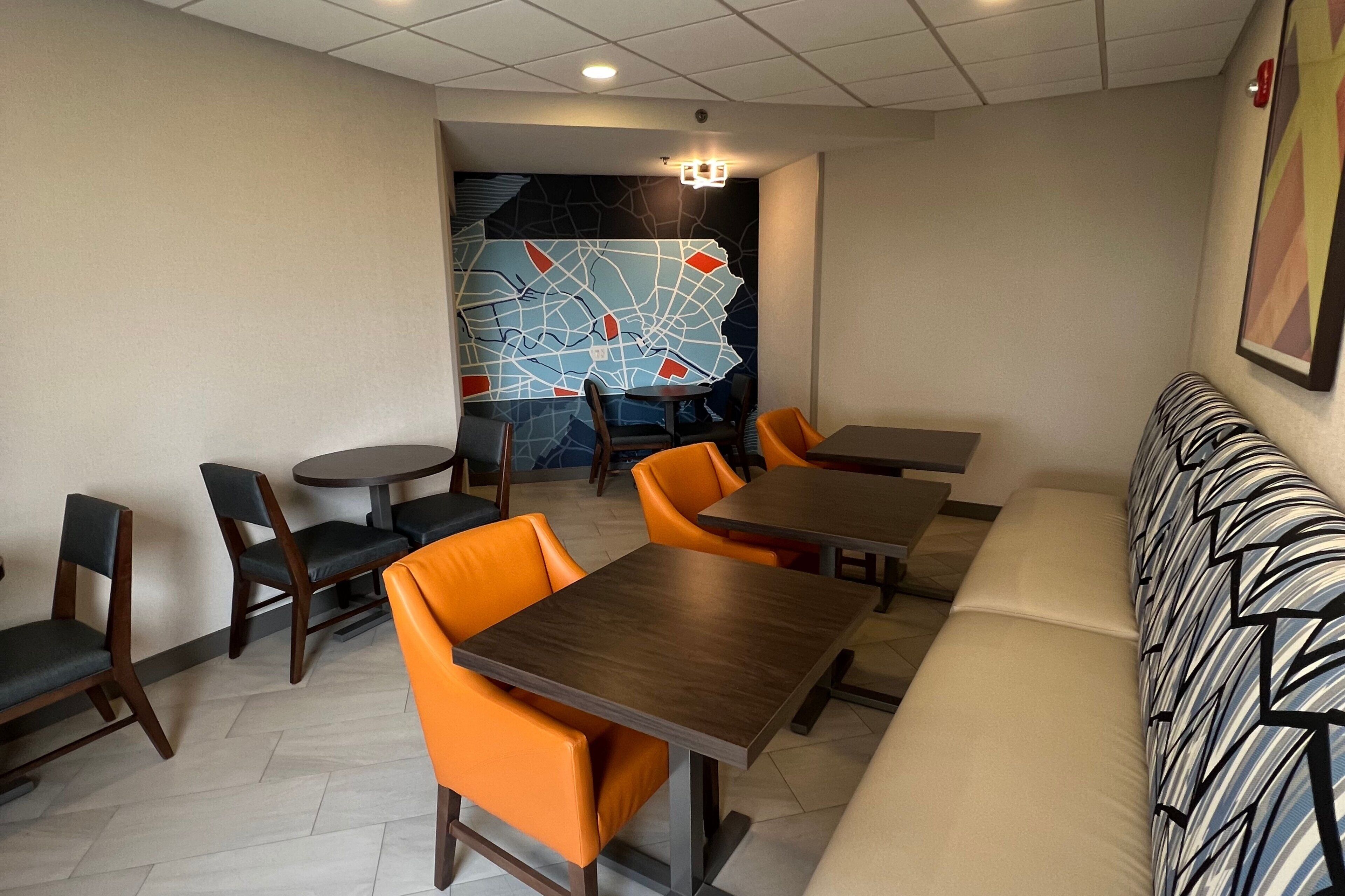 A restaurant with wooden tables and orange chairs, a map mural on the wall, and a patterned sofa.