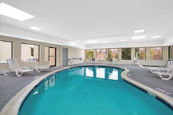 A swimming pool with multiple lounge chairs and a view of trees through large windows. - Holiday Inn Express Harrisburg I-81 – Hershey by IHG (Harrisburg)