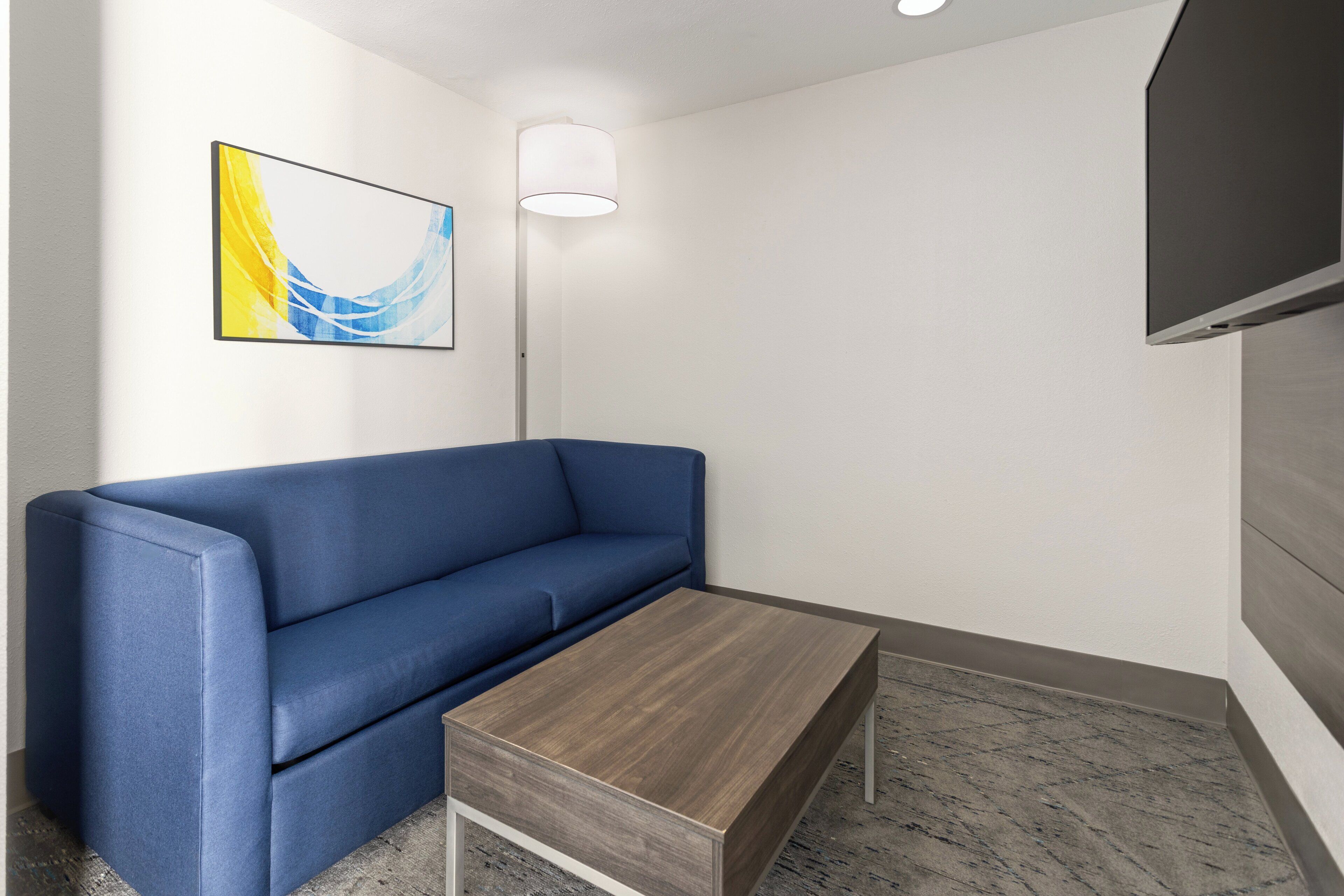 A modern room with a blue sofa, a wooden coffee table, a floor lamp, and a flat-screen TV mounted on the wall.