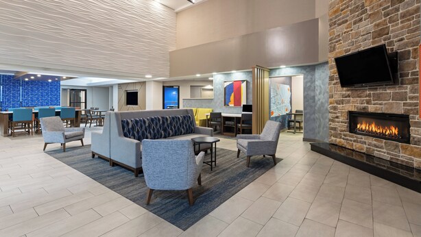 A modern lobby with seating areas, a fireplace, and a TV mounted on a stone wall. - Holiday Inn Express Harrisburg I-81 – Hershey by IHG (Harrisburg)