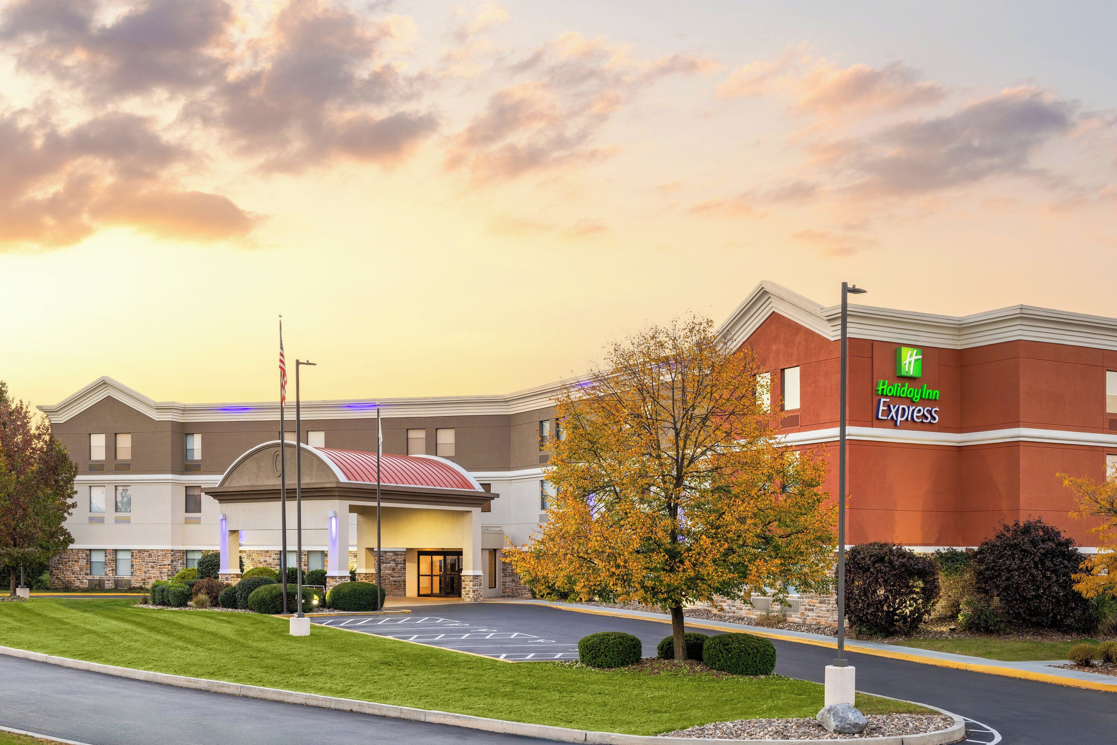 A Holiday Inn Express building with a brick facade, a red roof, and a parking lot with a tree in the foreground.
