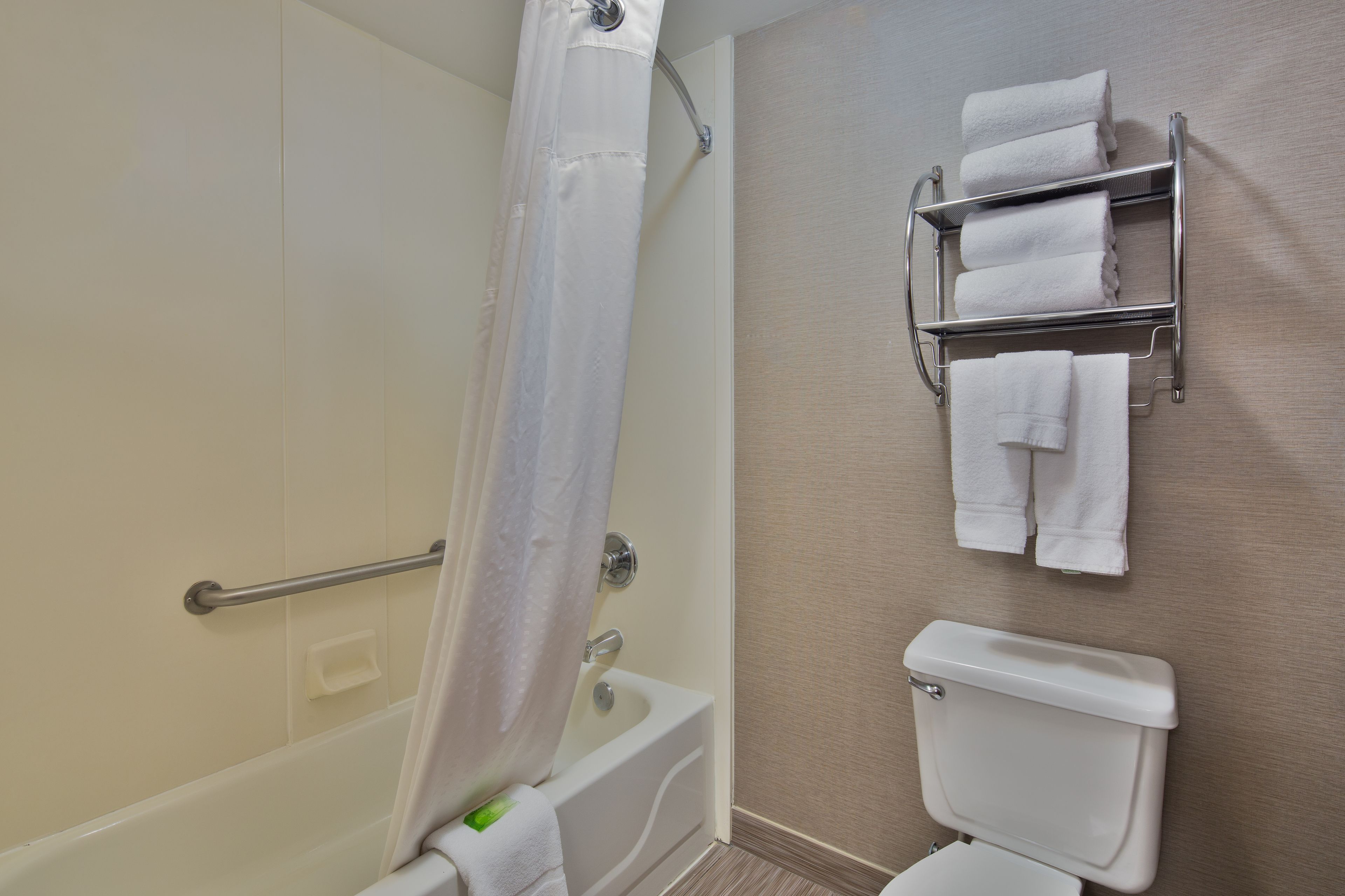 Un baño con bañera, inodoro y un perchero con varias toallas.