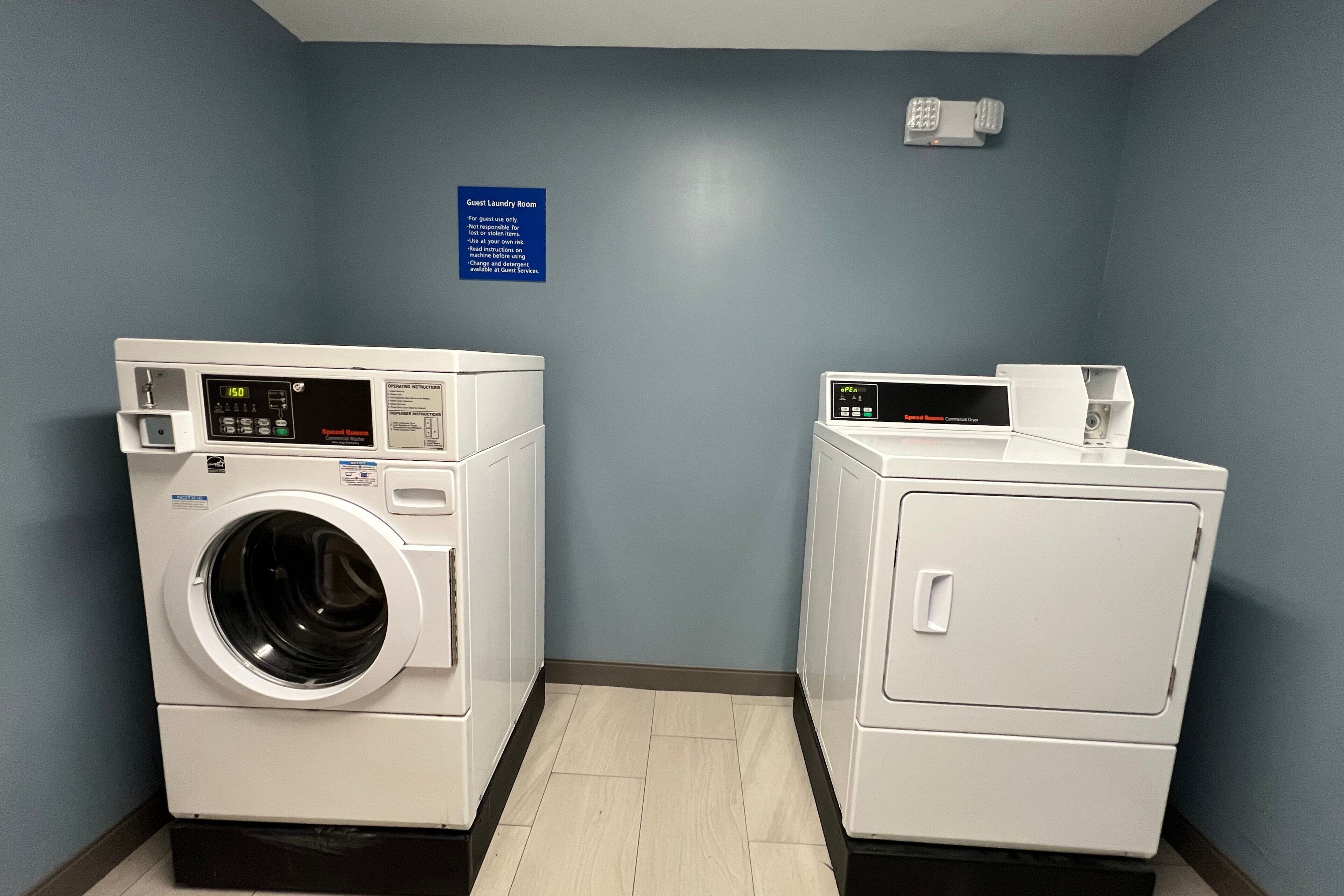 A laundry room with two washing machines and a dryer, a blue wall, and a sign indicating it's a guest laundry area.