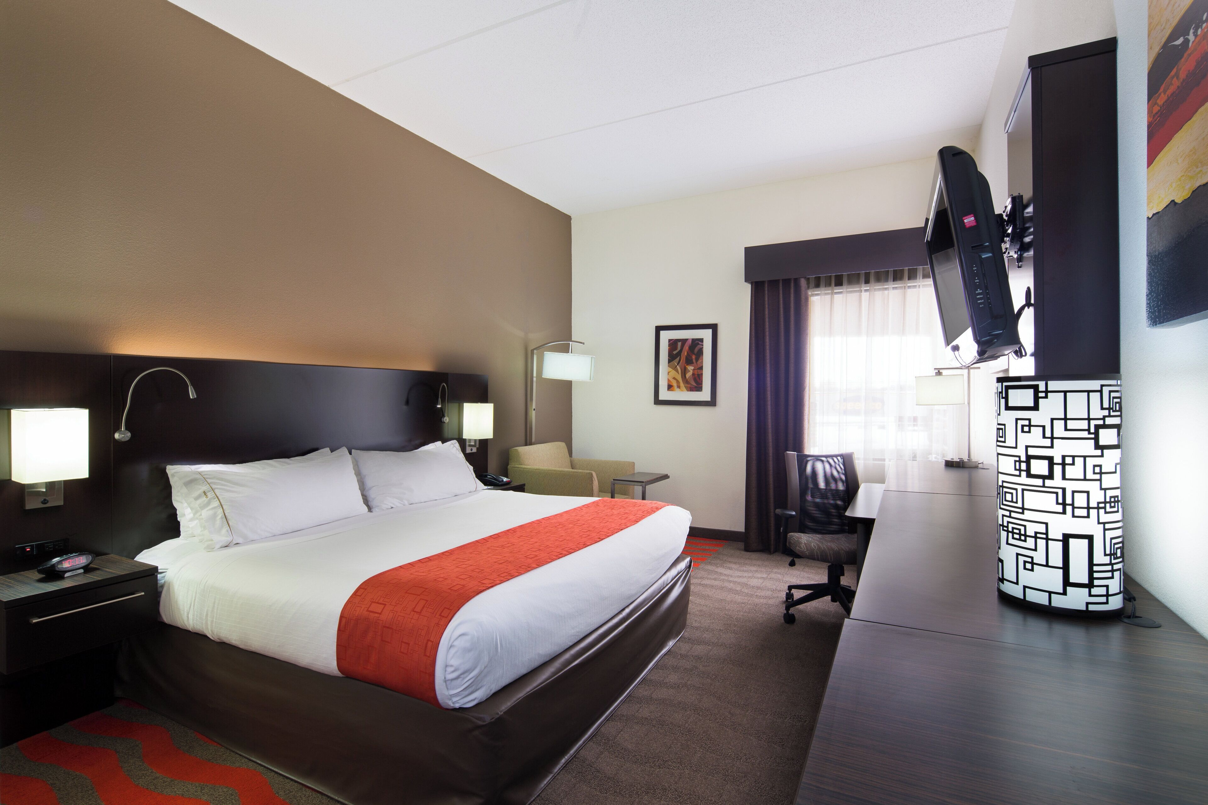 Habitación de hotel con cama, mesitas de noche, escritorio, silla, televisor y ventana con cortinas.