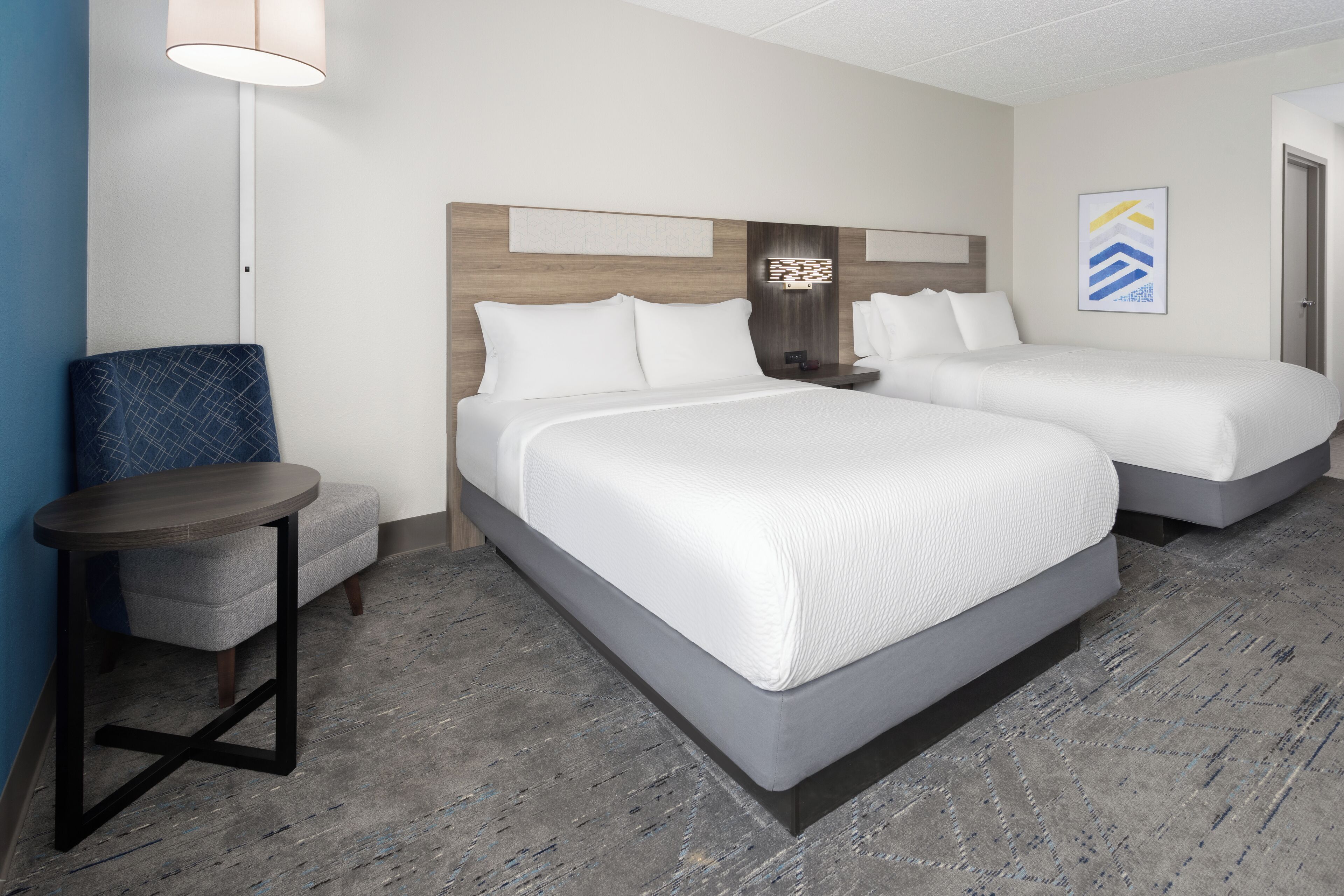 A hotel room with two beds, a small table, and a chair.