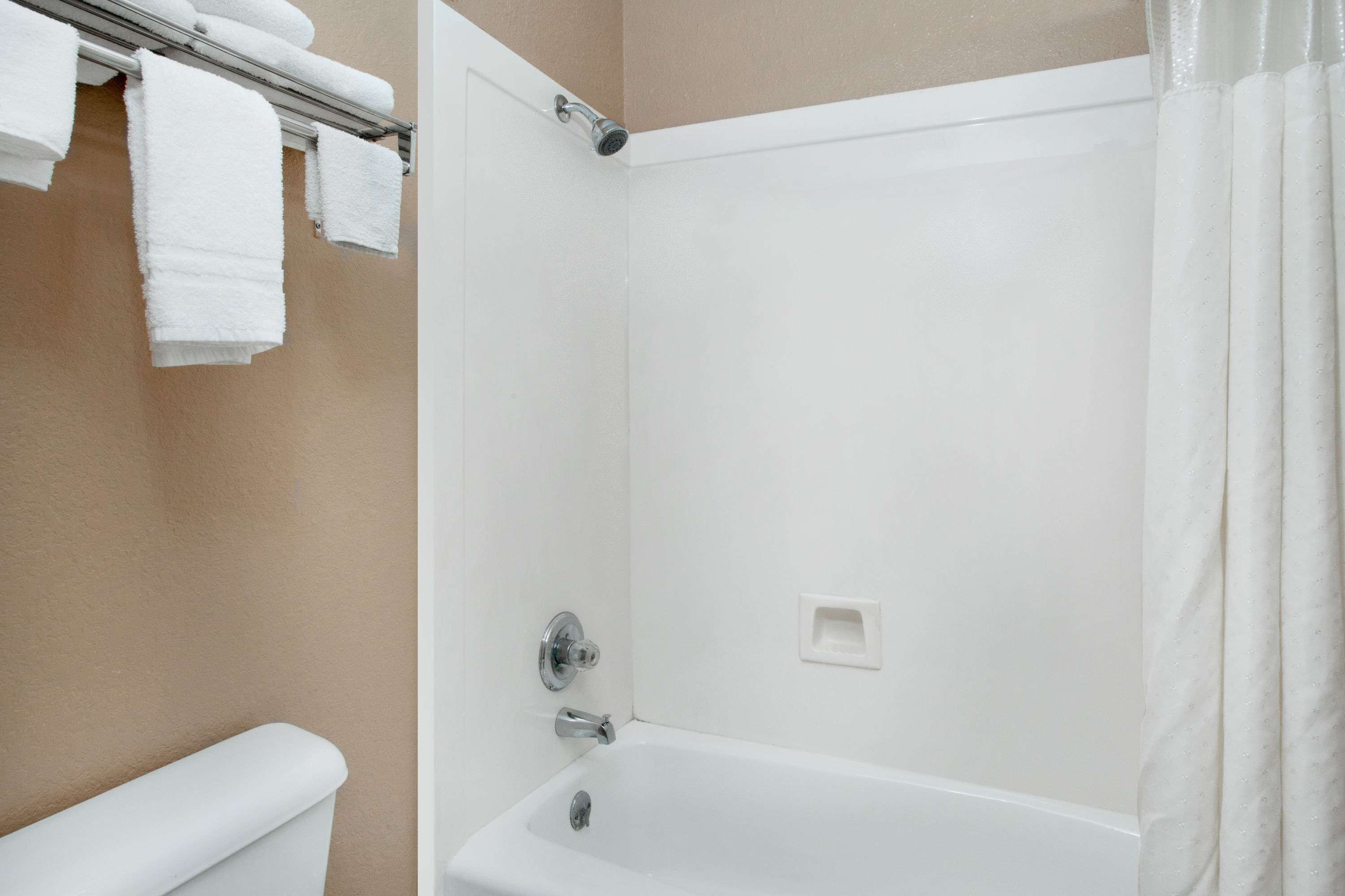 Un baño con bañera, un perchero con toallas blancas y una cortina de ducha.