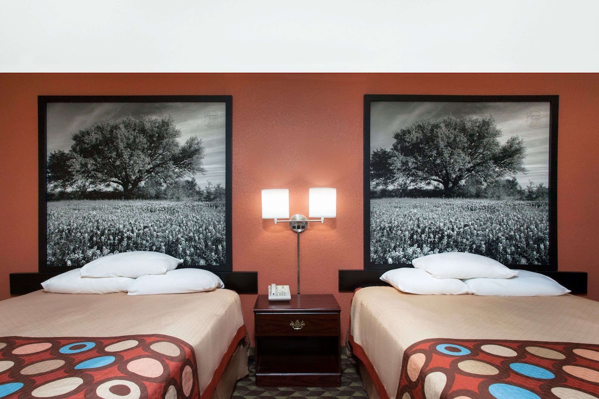 A hotel room with two beds, a nightstand, and a lamp.
