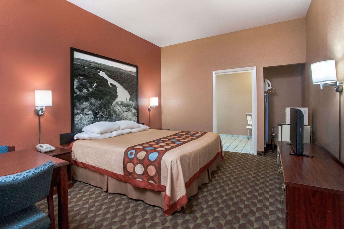A hotel room with a bed, desk, chair, desk lamp, and a large landscape painting.