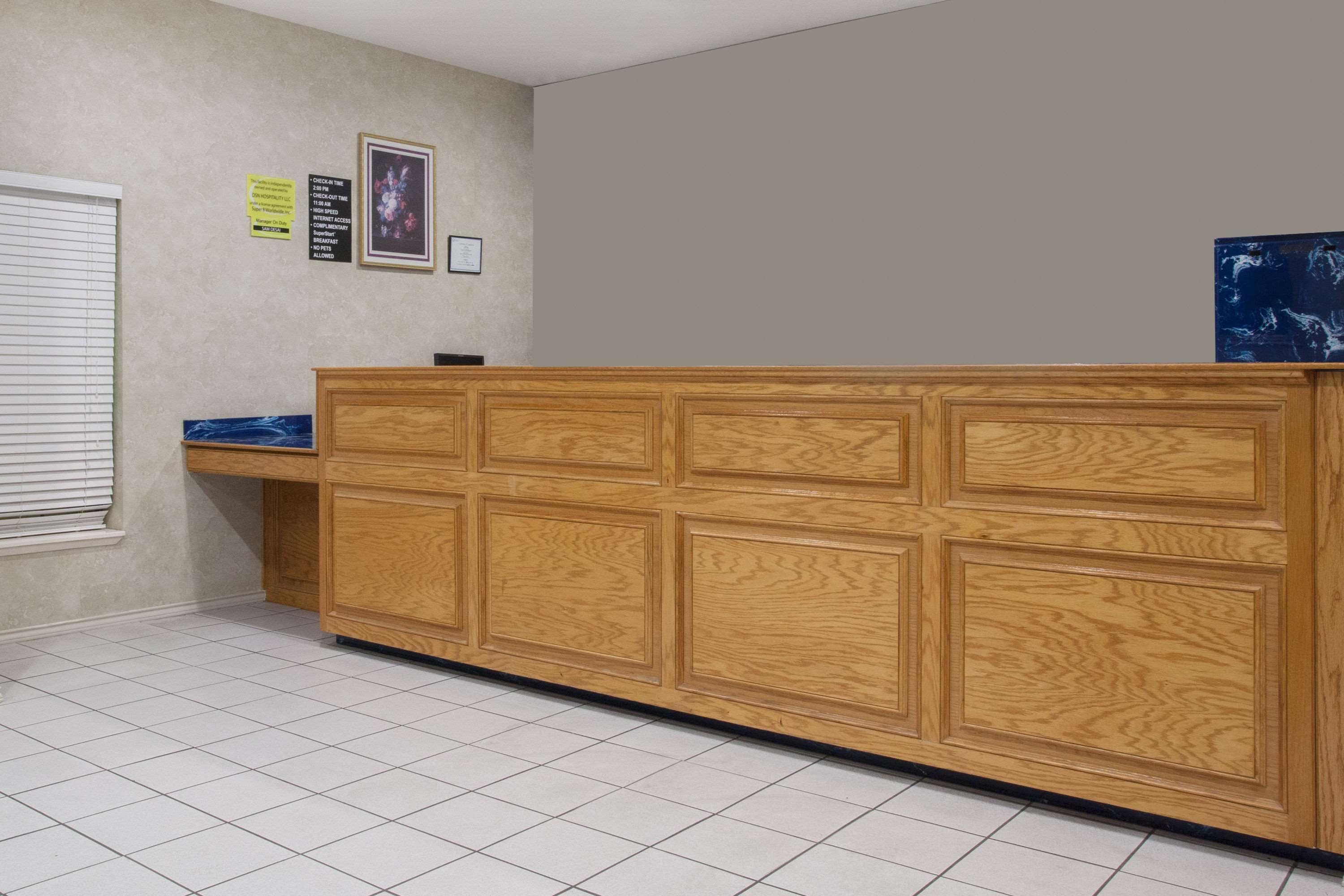 A reception area with a wooden reception desk, tiled floor, and a window with blinds.