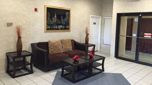 A lobby with a brown sofa, two side tables, a framed cityscape picture, and an exit sign.