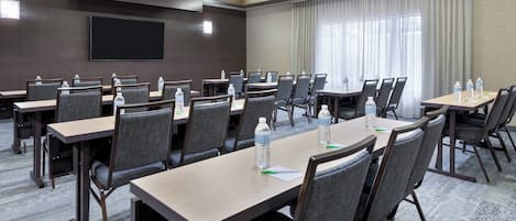 A hotel conference room with multiple tables and chairs, equipped with water bottles and notepads.