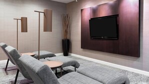 A modern living room with a flat-screen TV mounted on a wooden wall, grey upholstered sofas, a coffee table, and floor lamps.