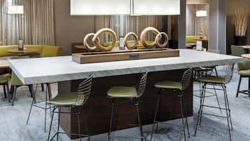 A modern bar area with a marble countertop, green cushioned bar stools, and a decorative wooden centerpiece.