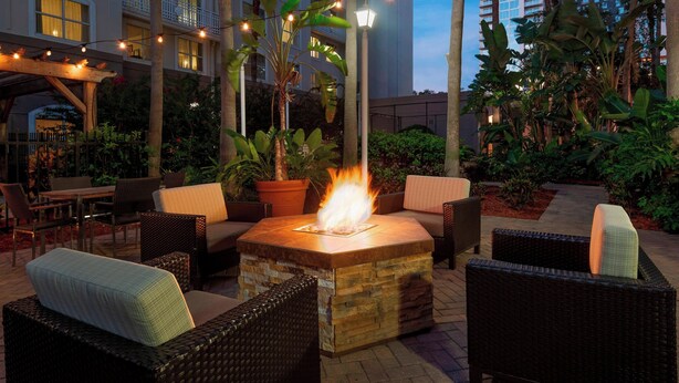 An outdoor patio area with a central fire feature, wicker furniture, and string lights.