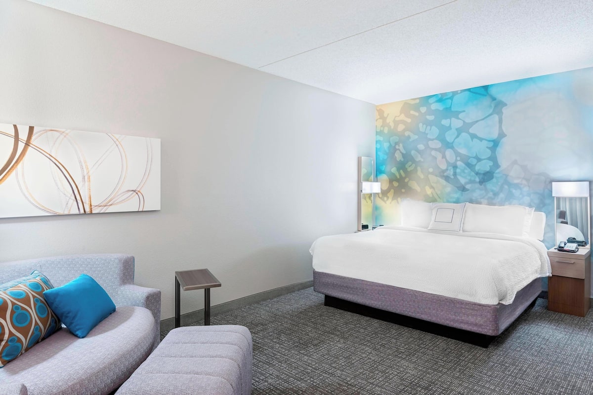Une chambre d’hôtel avec un lit, un canapé, une petite table et un mur décoré d’œuvres d’art abstraites.