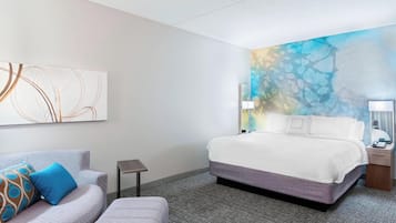 A hotel room with a bed, a sofa, a small table, and a wall with abstract art.
